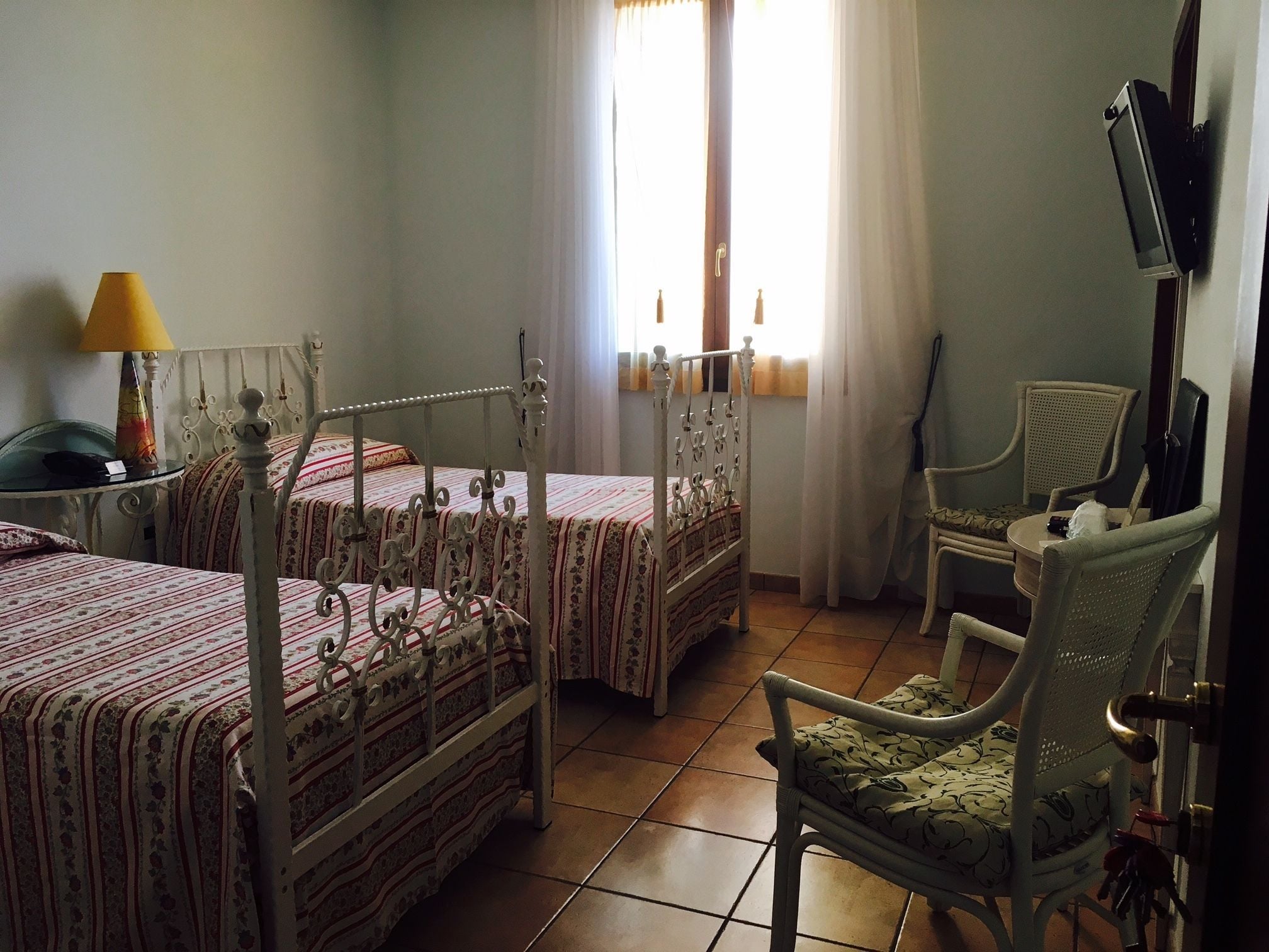Una habitación con dos camas, una silla, un televisor y un ventanal con cortinas.