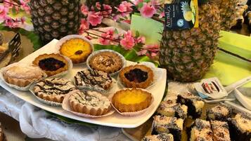 Una mesa de bufé con diversos postres, como tartas, pasteles y productos de pastelería, rodeada de piñas y flores.