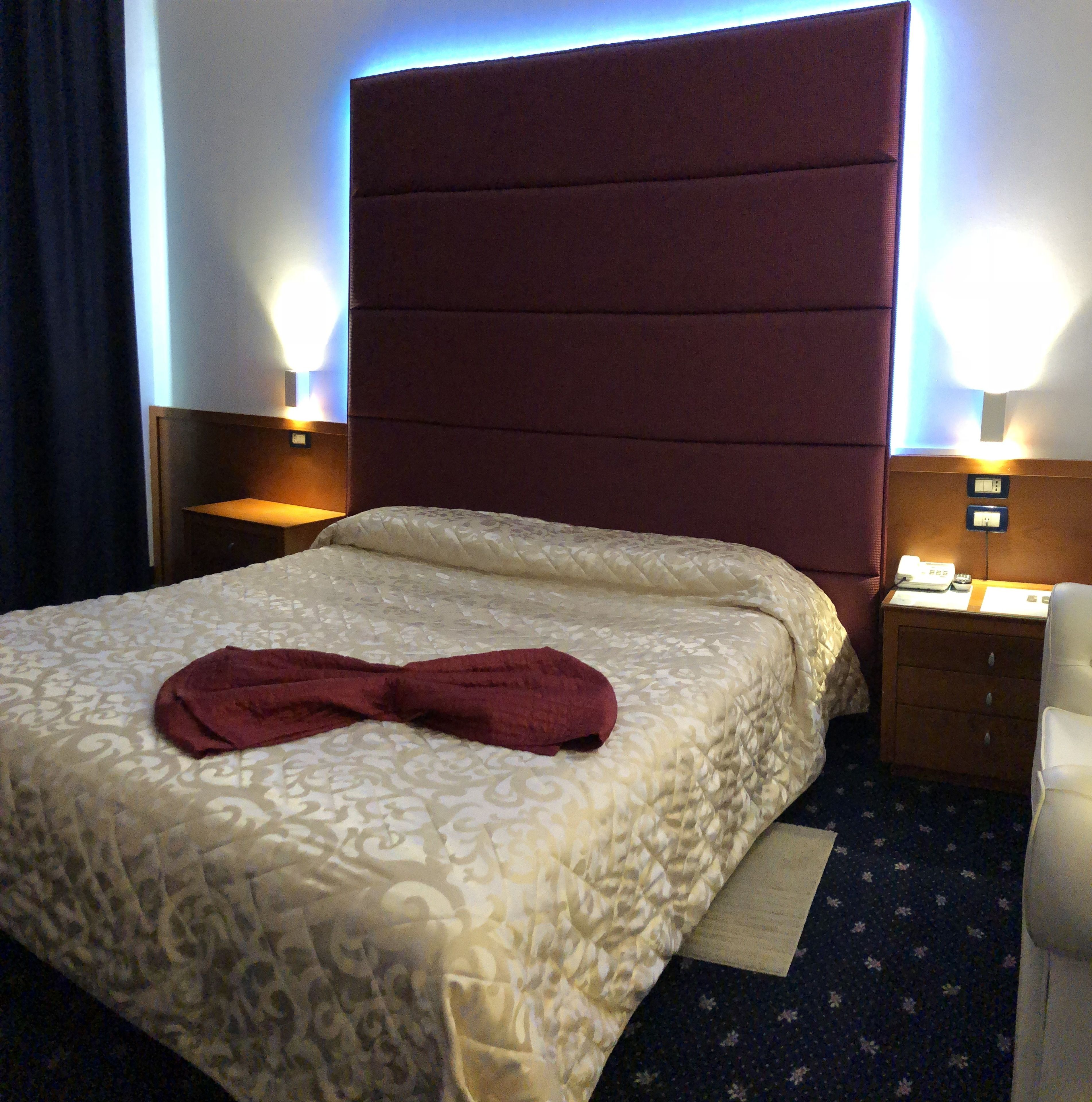 Ein Hotelzimmer mit einem großen Bett, einem Kopfteil, zwei Nachttischen inklusive Lampen und einem kleinen Beistelltisch.