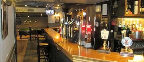 Un área de bar con mostrador, taburetes y una pantalla de televisión.