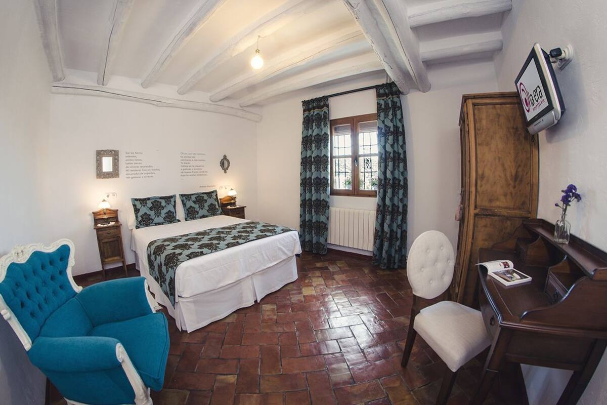 Een slaapkamer met een bed, een blauwe fauteuil, een houten bureau en een stoel.