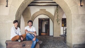 Deux personnes sont assises sur un banc en bois, à l’abri d’une structure en pierre en forme d’arche.