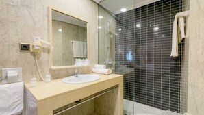 A modern bathroom with a marble vanity, a large mirror, a handheld showerhead, and a glass-enclosed shower area. - Apartamentos Torreluz (Almeria)