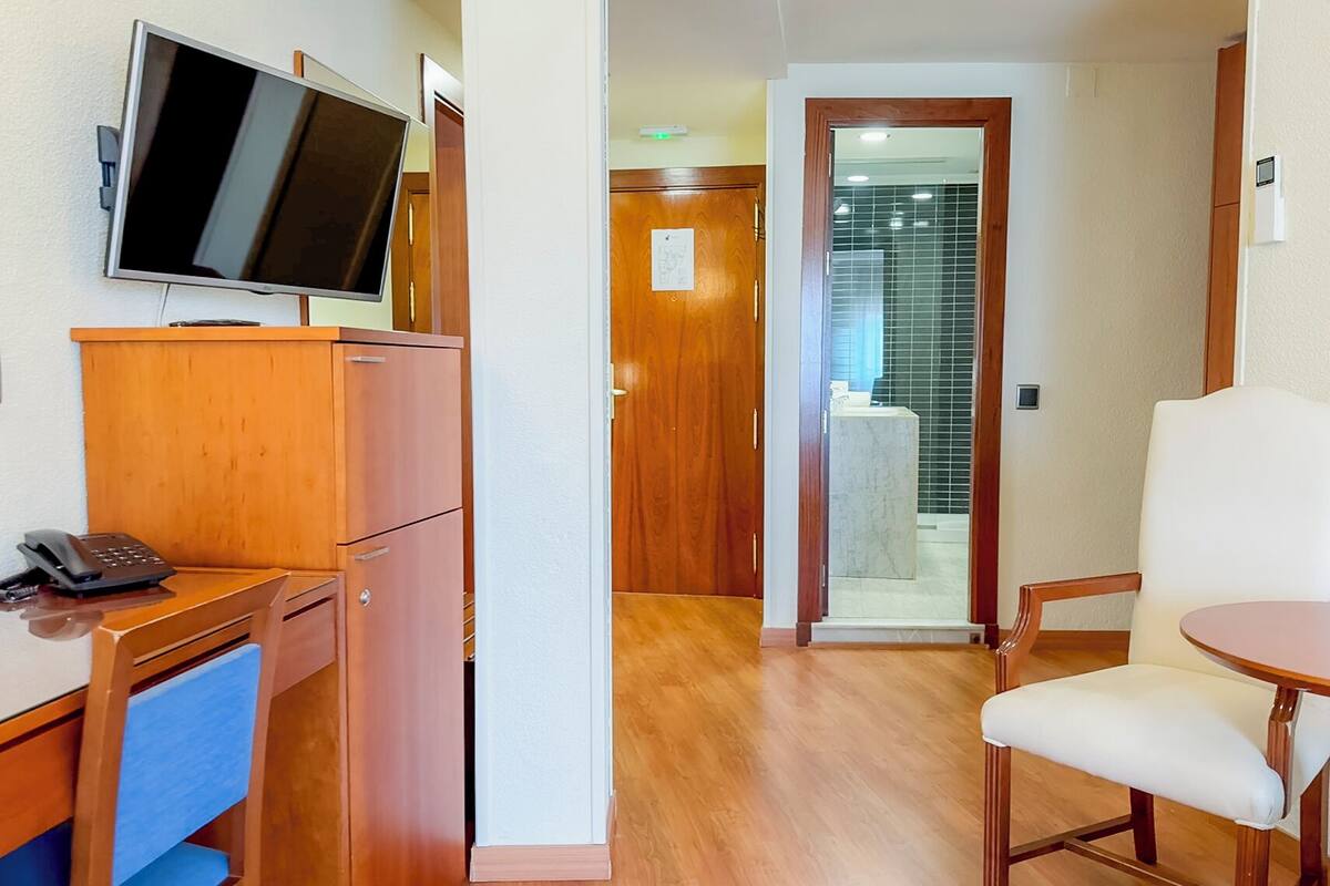 Hotelkamer met een houten bureau, een flatscreen televisie, een telefoon, een stoel en een douchecabine van glas.