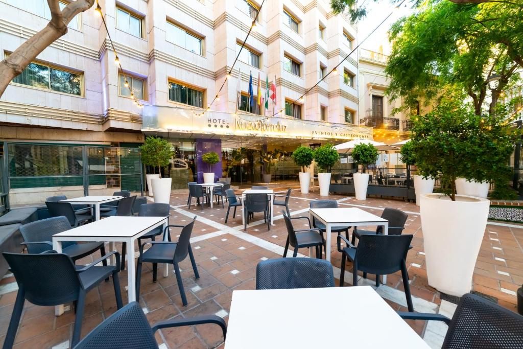 Un área de patio al aire libre con mesas y sillas, un edificio con un letrero que dice 'Hotel Nuevo Horizonte' y banderas.