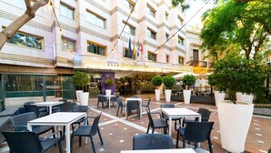 Un área de patio al aire libre con mesas y sillas, un edificio con un letrero que dice 'Hotel Nuevo Horizonte' y banderas.