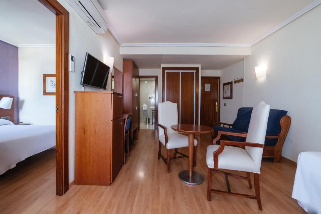 Una habitación de hotel con cama, televisión, una mesa de comedor con sillas y un sofá.