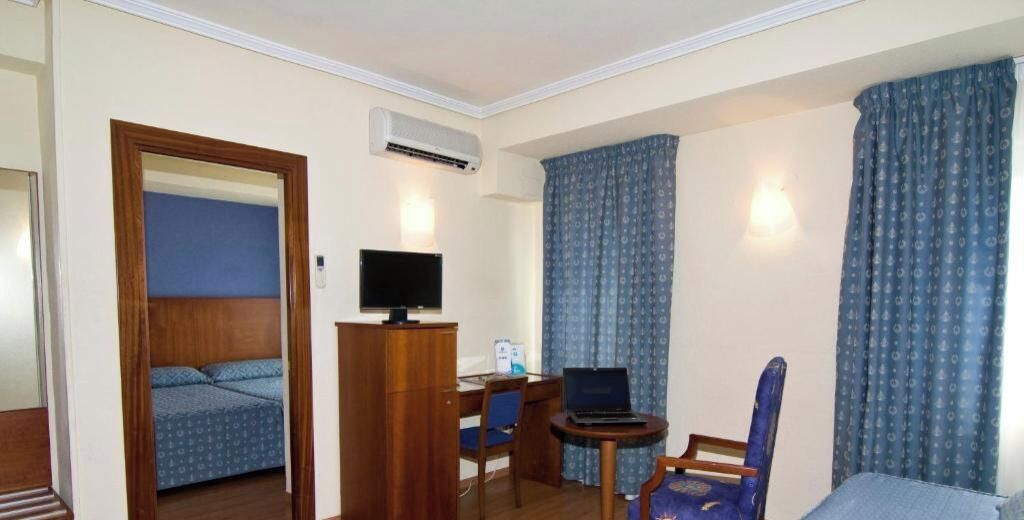 Una habitación de hotel con una cama, un escritorio con una computadora portátil, una silla y cortinas.