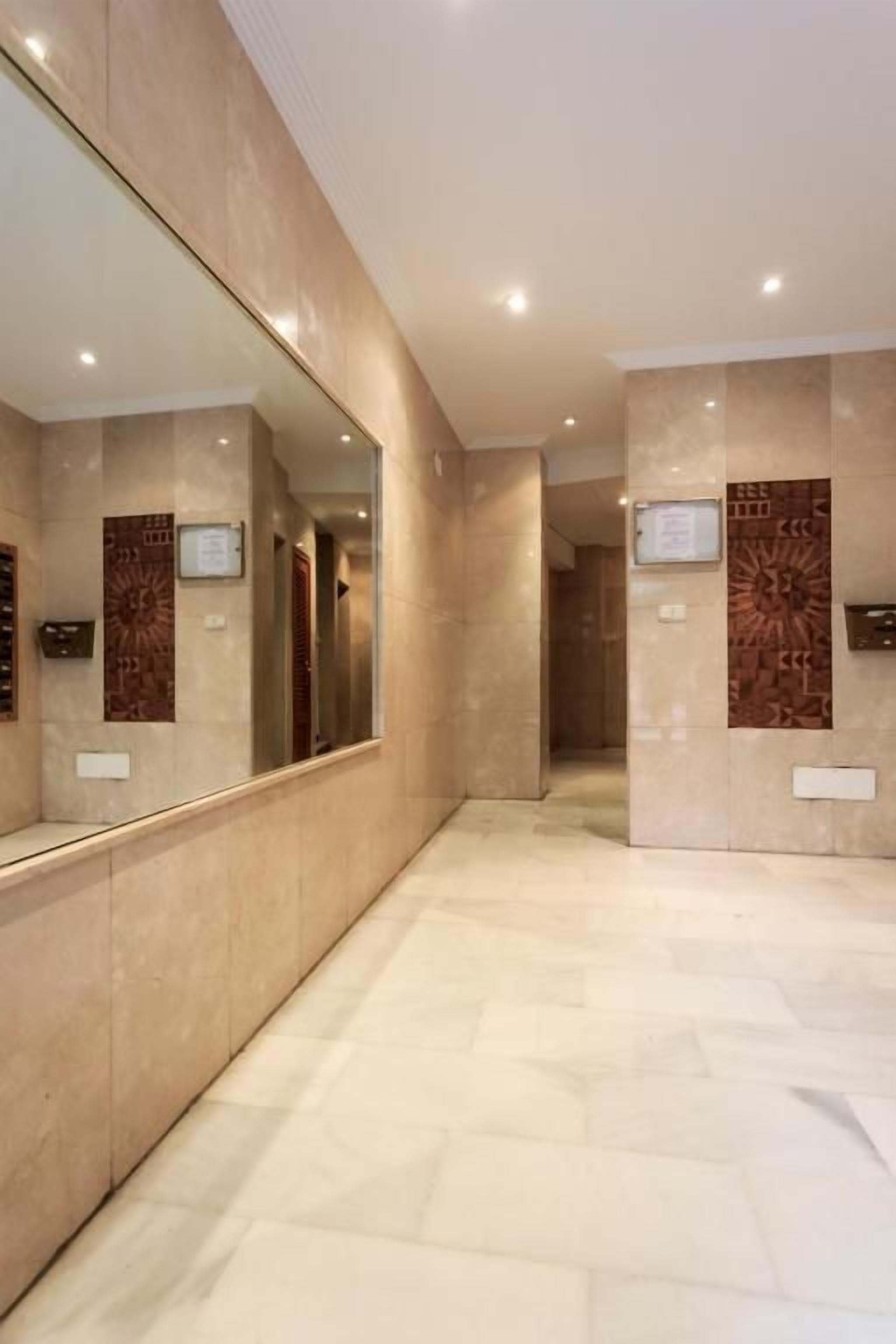 A corridor with a reflective wall and a patterned wall, leading to a door.