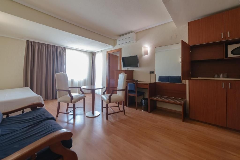 Habitación de hotel con cama, escritorio, silla, televisor y armario.