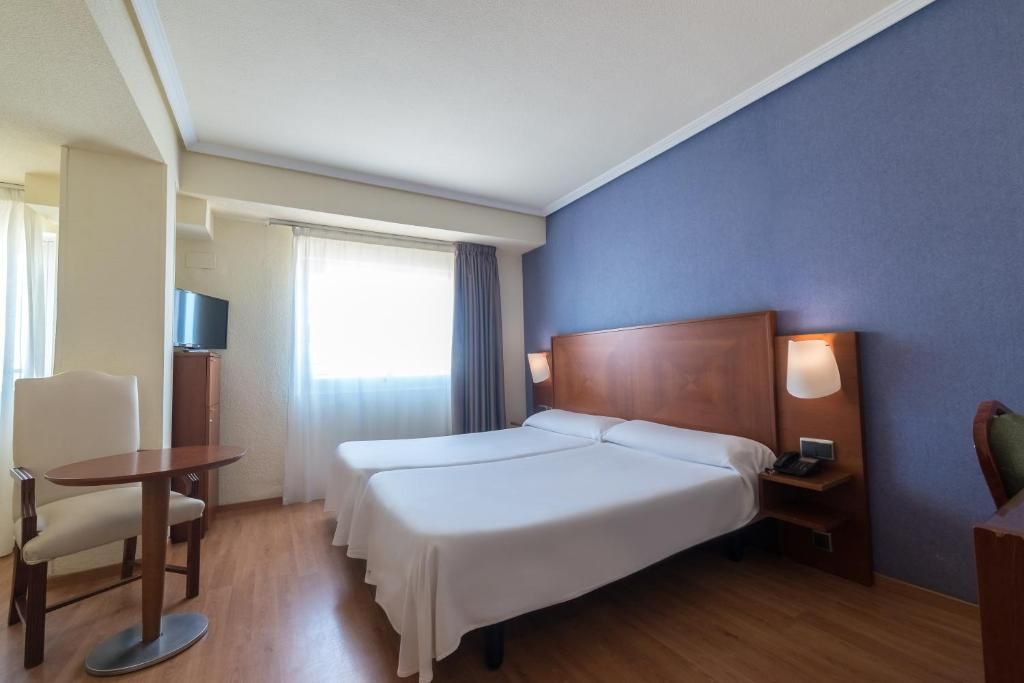 Camera d'albergo con due letti, una scrivania, una sedia, una televisione e una finestra con tende.