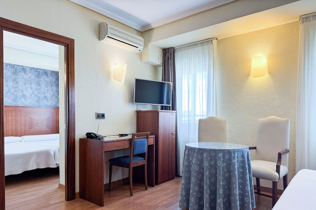 Een hotelkamer met een bed, een bureau met stoel, een televisie en een kleine tafel met twee stoelen.