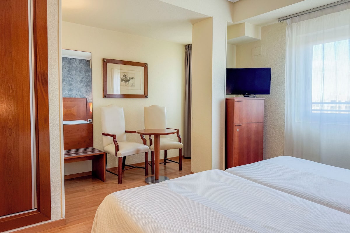 Een hotelkamer met een bed, bureau, twee stoelen, televisie en een kast.