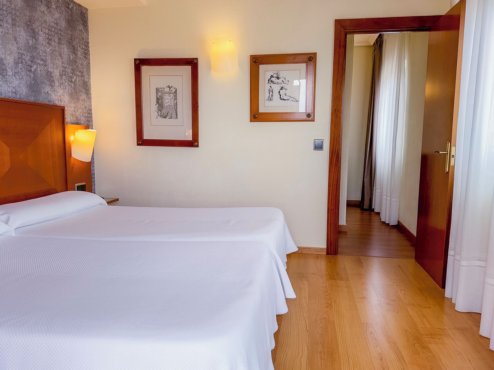 Habitación de hotel con una cama grande, dos cuadros en la pared, cabecera de madera y suelo de madera.