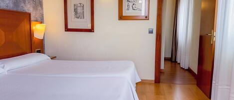 Habitación de hotel con una cama grande, dos cuadros en la pared, cabecera de madera y suelo de madera.