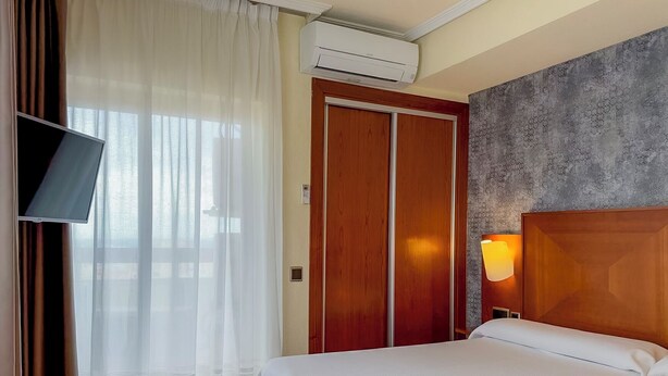 A hotel room with a bed, a TV, an air conditioner, and a wooden wardrobe. - Apartamentos Torreluz (Almeria)
