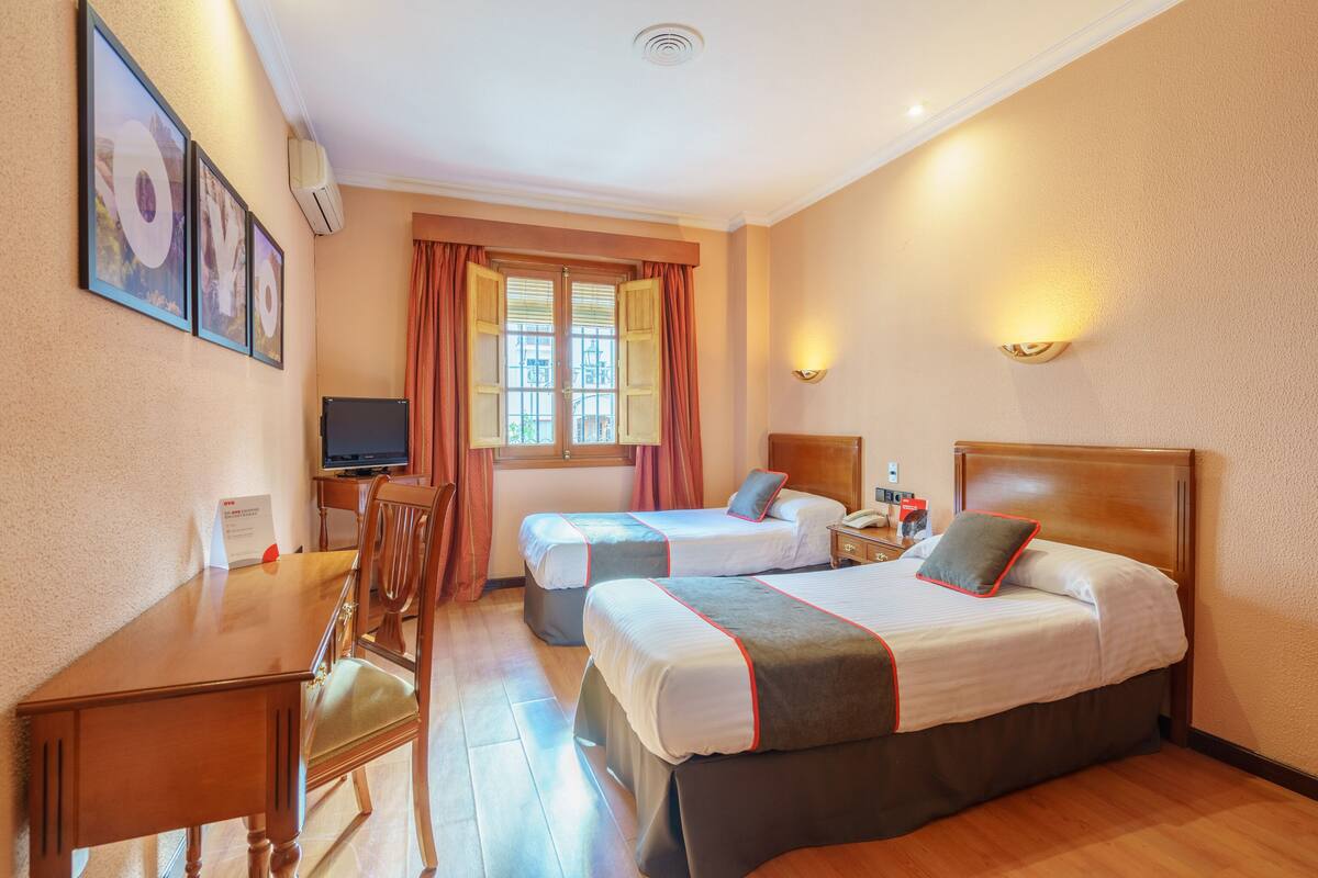 Habitación de hotel con dos camas, un escritorio, una silla, un televisor y una ventana con cortinas.