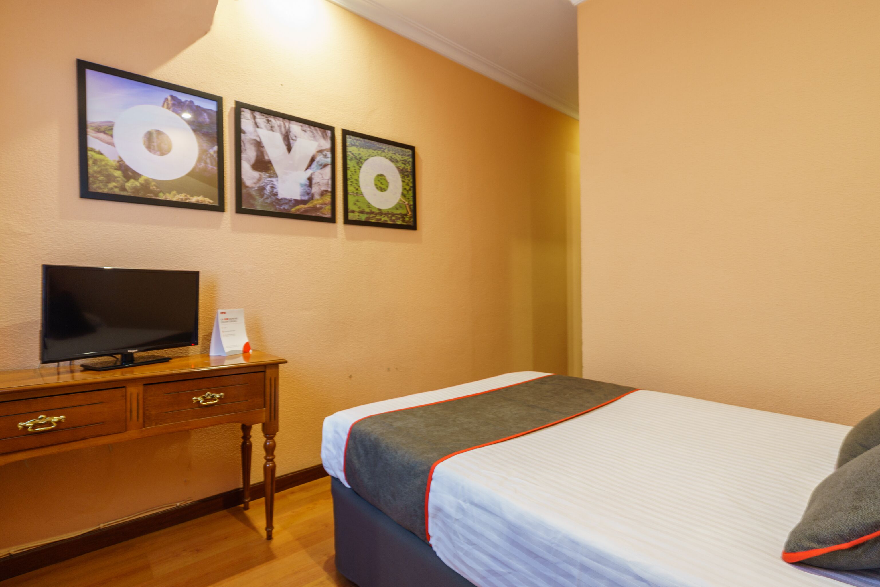 A hotel room with a bed, a TV on a wooden dresser, and three framed pictures on the wall.