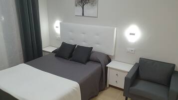 A bedroom with a bed, two bedside tables, a chair, and a wall-mounted light fixture.