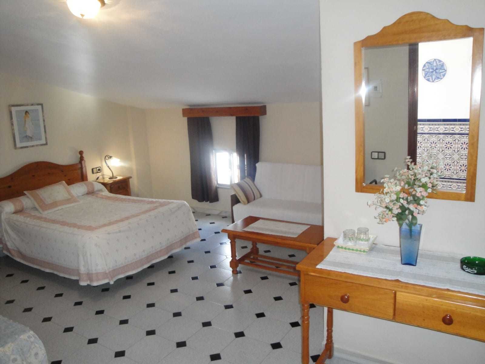 A hotel room with a bed, a desk, a chair, a mirror, and a window with curtains.