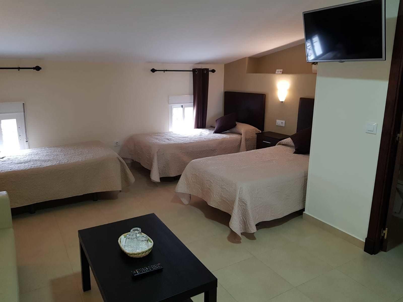 Una habitació d'hotel amb dos llits individuals, un televisor penjat a la paret, una taula petita amb un objecte decoratiu i una finestra que ofereix llum natural.