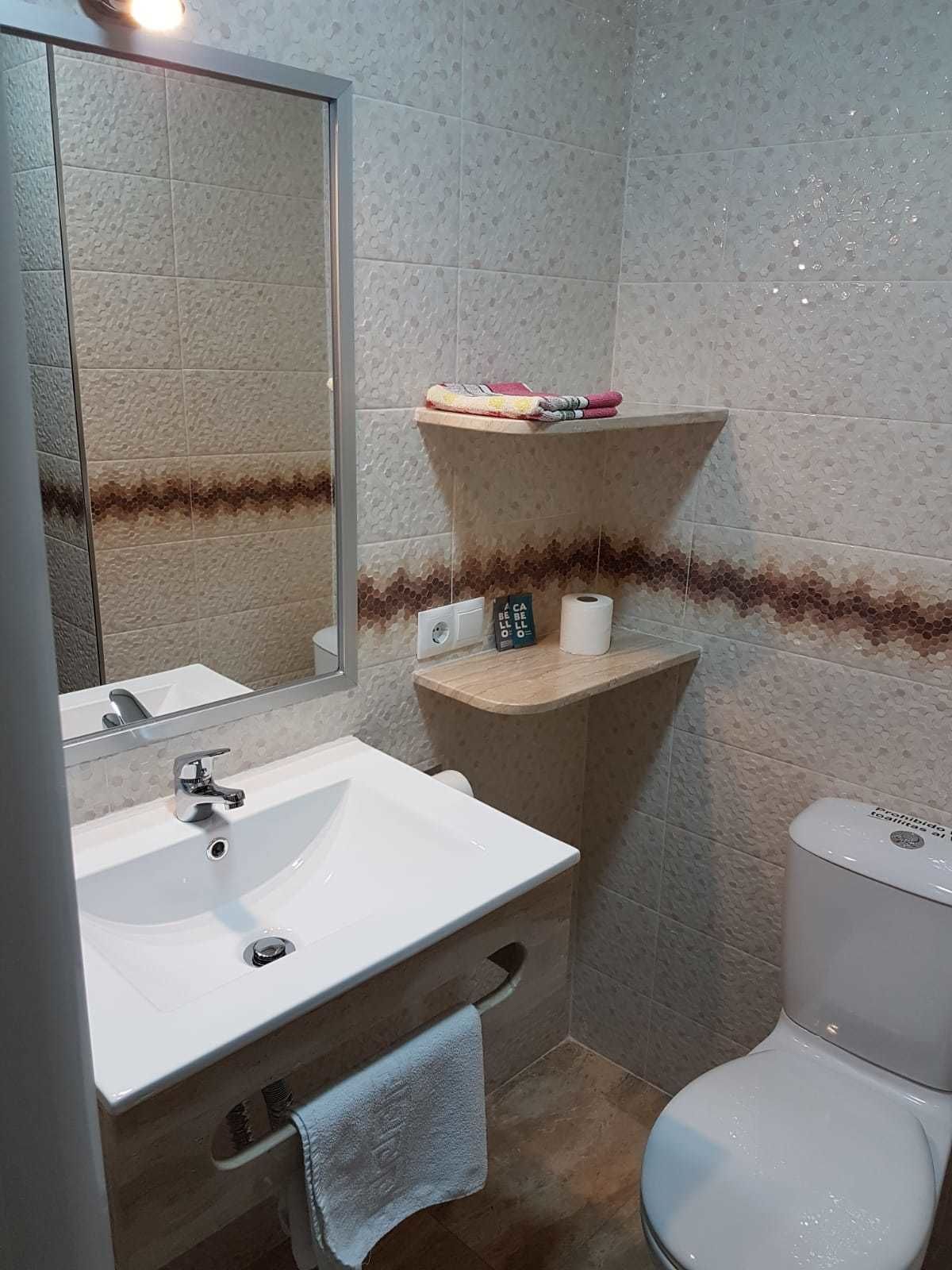 A bathroom with a white sink, a mirror, a toilet, and a shelf with toiletries.