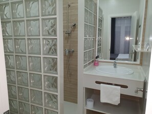 Une salle de bain avec une douche à parois de verre, un lavabo blanc avec un miroir et une serviette accrochée au mur.