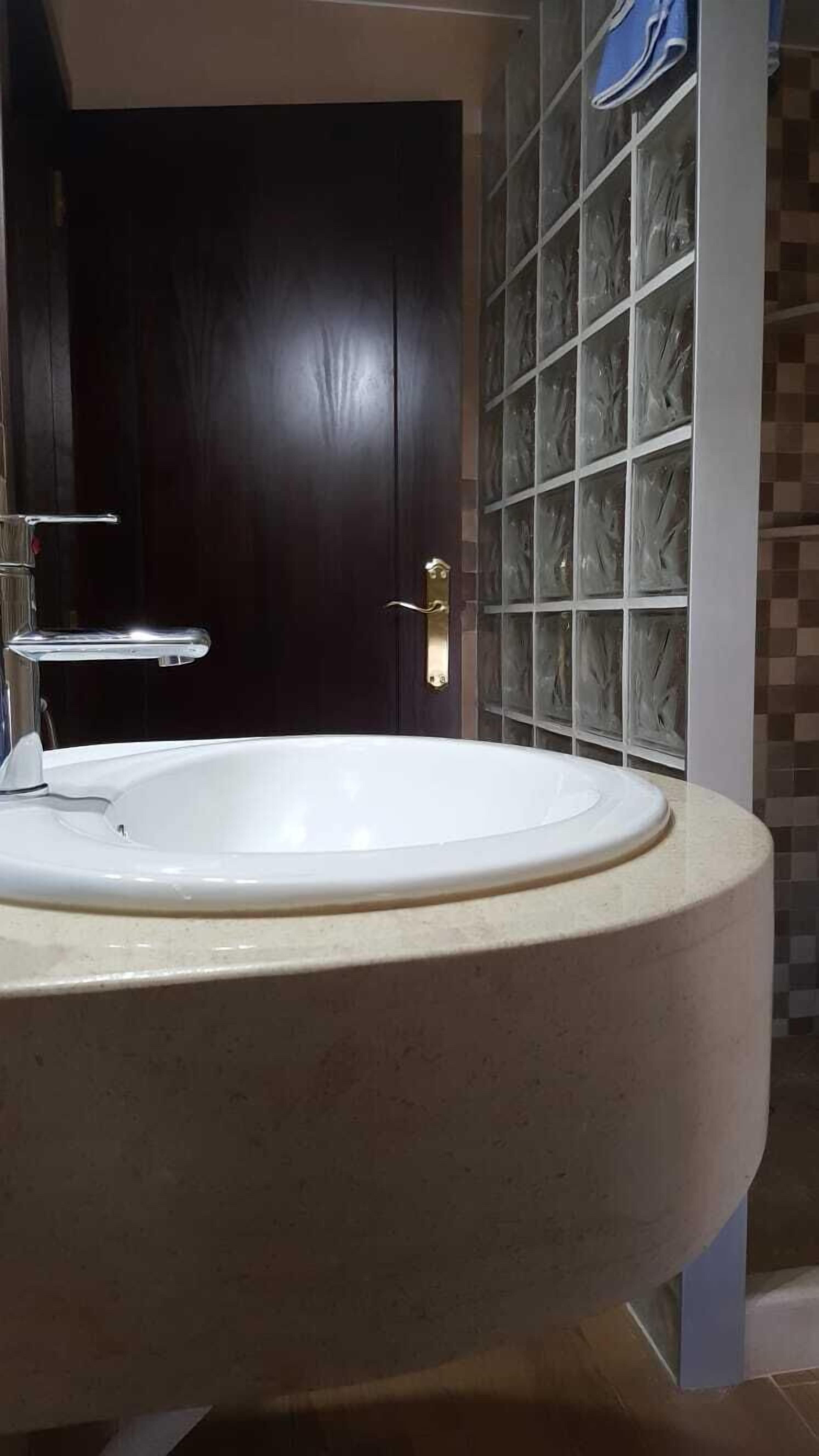 Un baño con un lavamanos blanco, una puerta de madera oscura y una pared con azulejos y diseño de bloques de vidrio.