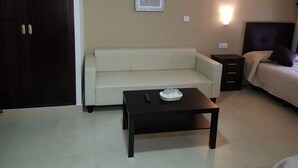 A small, well-lit room with a sofa, a small table, a bed with a headboard, and a wall-mounted light. - Hostal Málaga (Arcos de la Frontera)