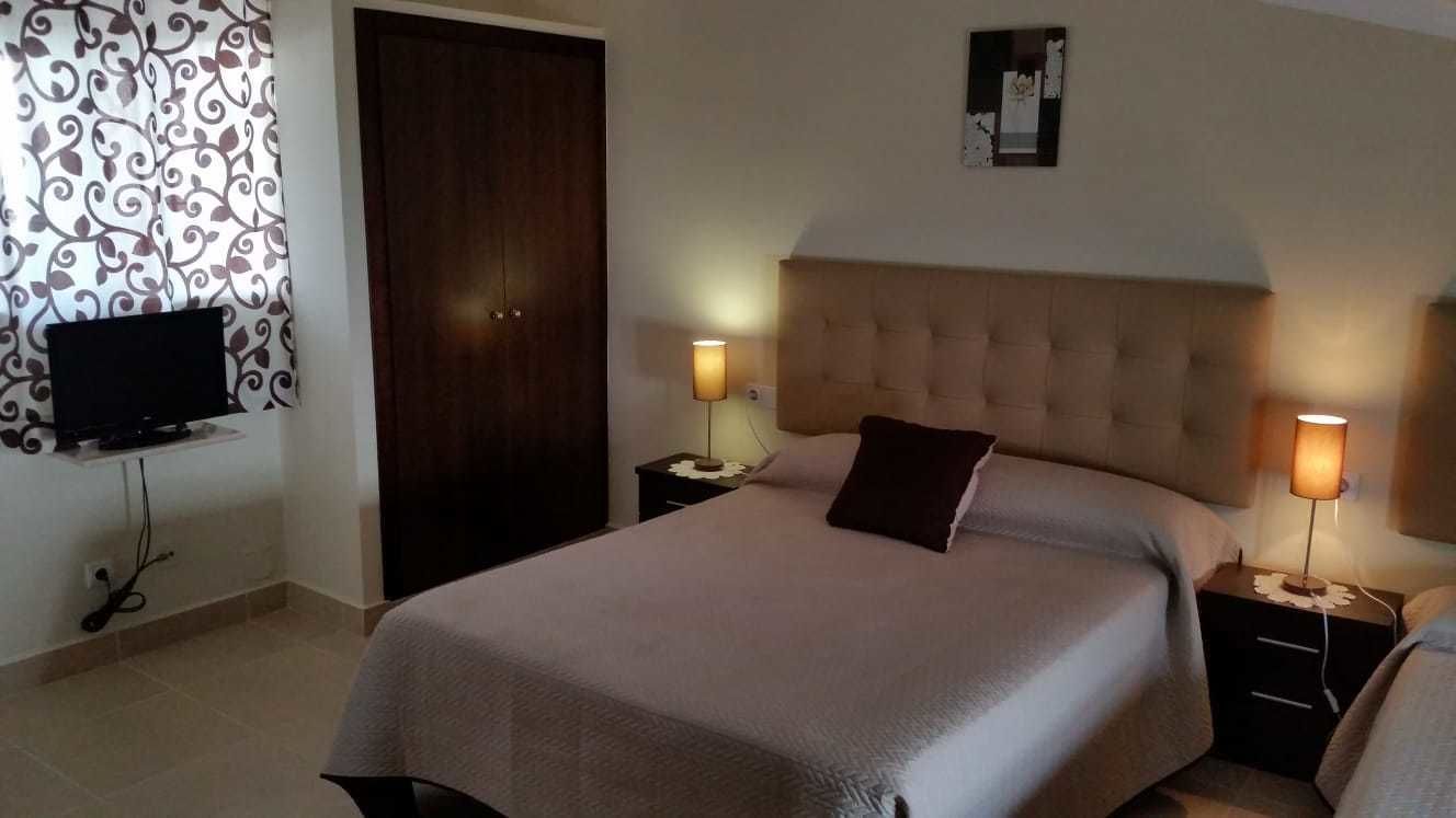 Une chambre à coucher avec un grand lit, deux tables de chevet avec des lampes, un téléviseur posé sur un meuble, une porte et un rideau à motifs.