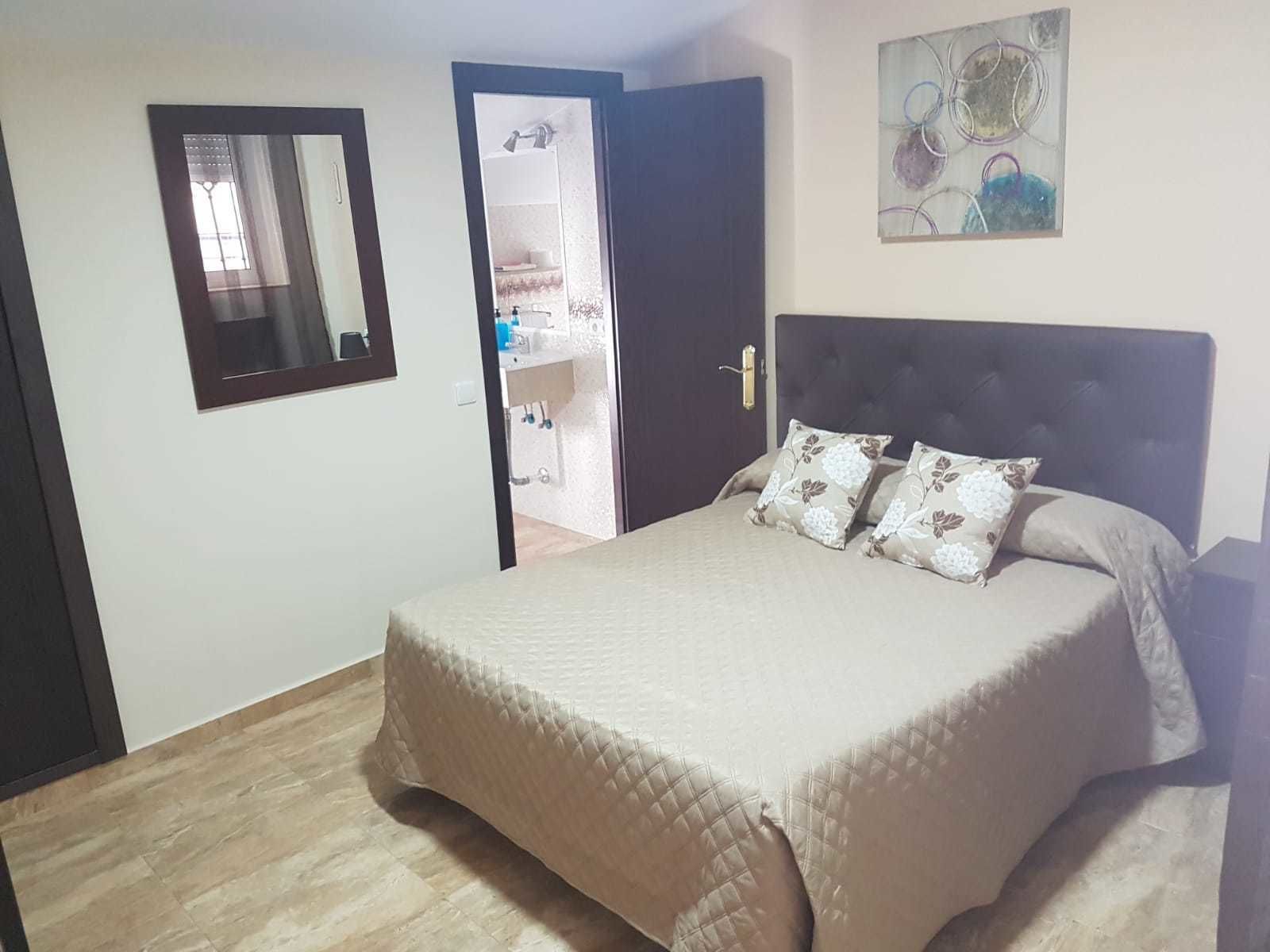 A bedroom with a bed, a door leading to a bathroom, and a wall-mounted mirror.