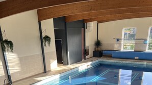 Une piscine intérieure dotée d’un sol carrelé et d’un plafond en bois.