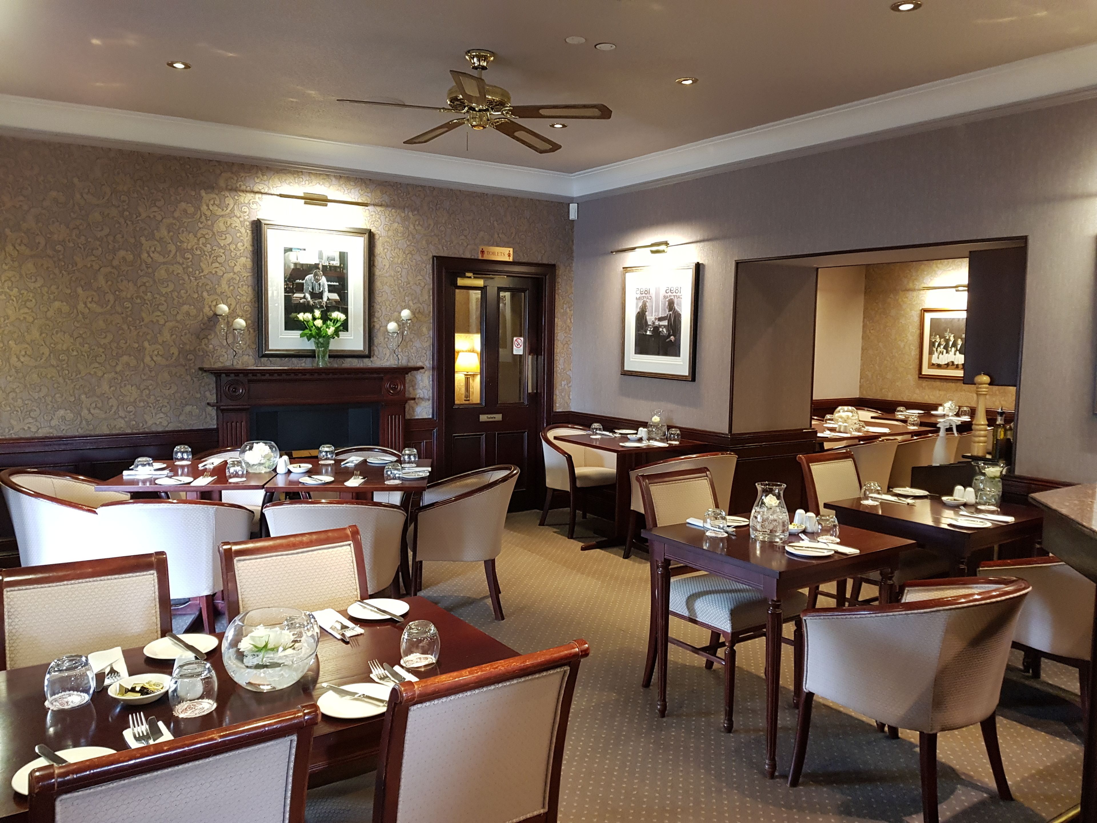 A dining area with multiple tables set for service, a fireplace, and framed pictures on the walls.