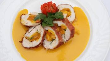 Un plato con rodajas de pechuga de pollo rellena, cilantro como guarnición y un pimiento rojo.