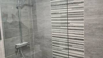 A modern shower area with a glass partition, a handheld showerhead, and a wall-mounted faucet.