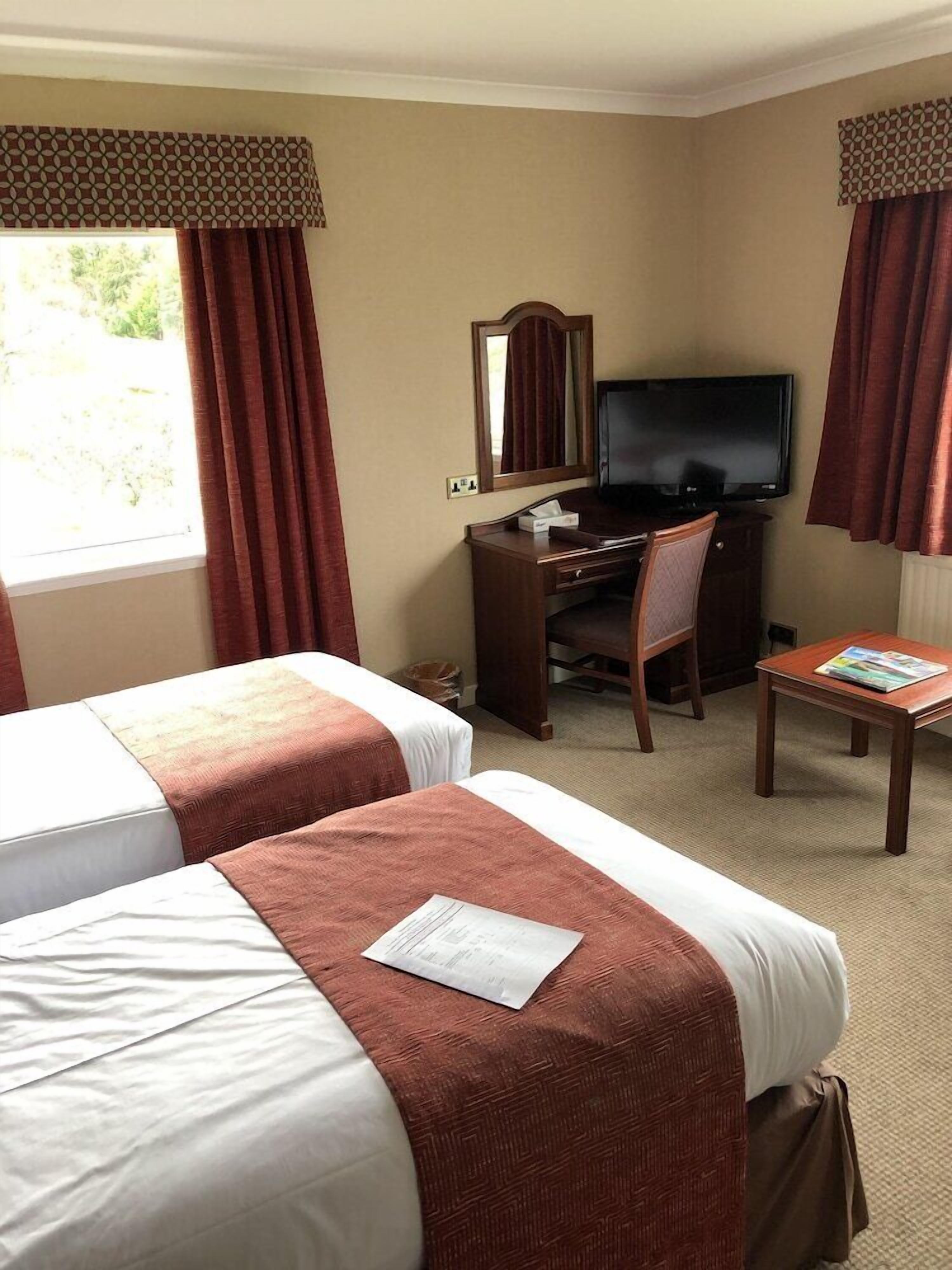A hotel room with two beds, a desk with a computer, a TV, and a small table with a magazine.