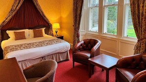 A hotel room with a four-poster bed, a sitting area with two leather armchairs and a table, and a large window with curtains. - Ramnee (Forres)