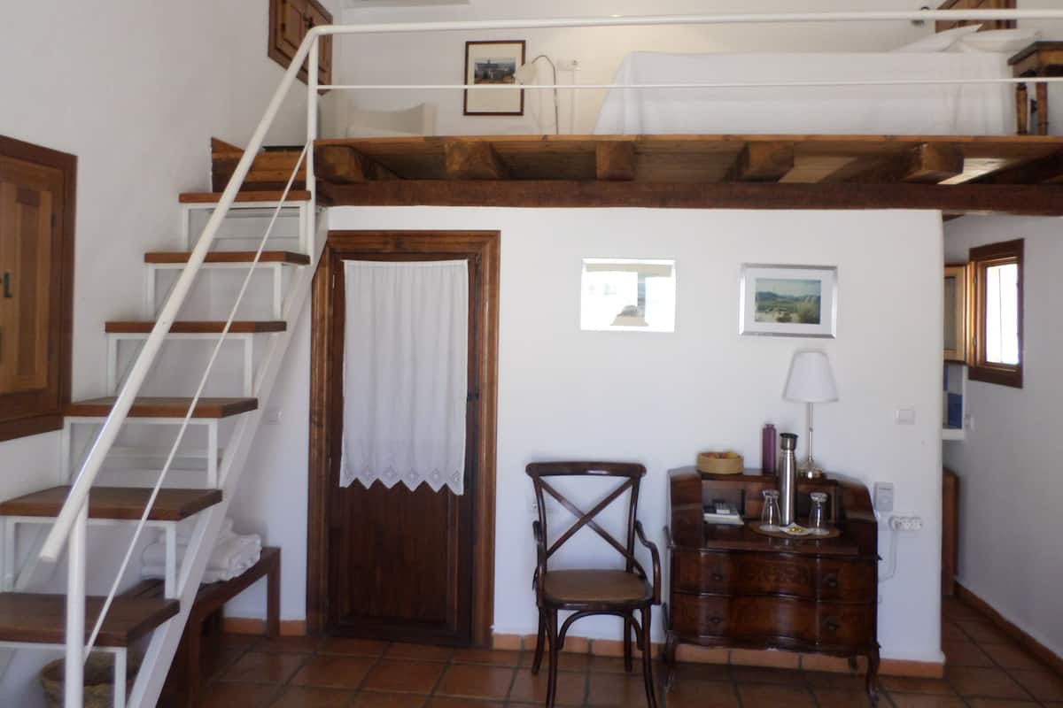 A room with a wooden staircase, a chair, a dresser, and a window.