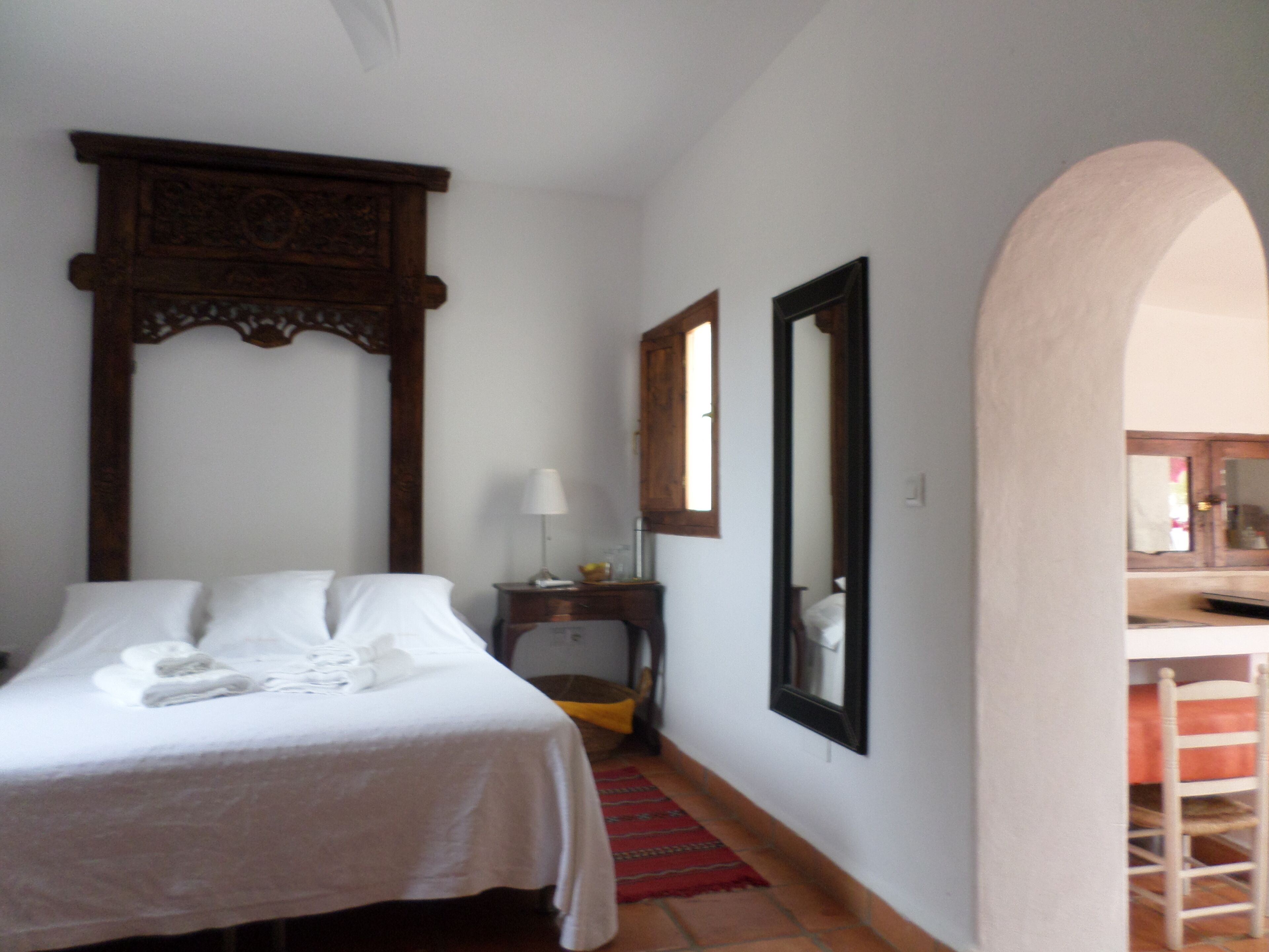 A hotel room with a bed, a nightstand, a mirror, and a wooden headboard.