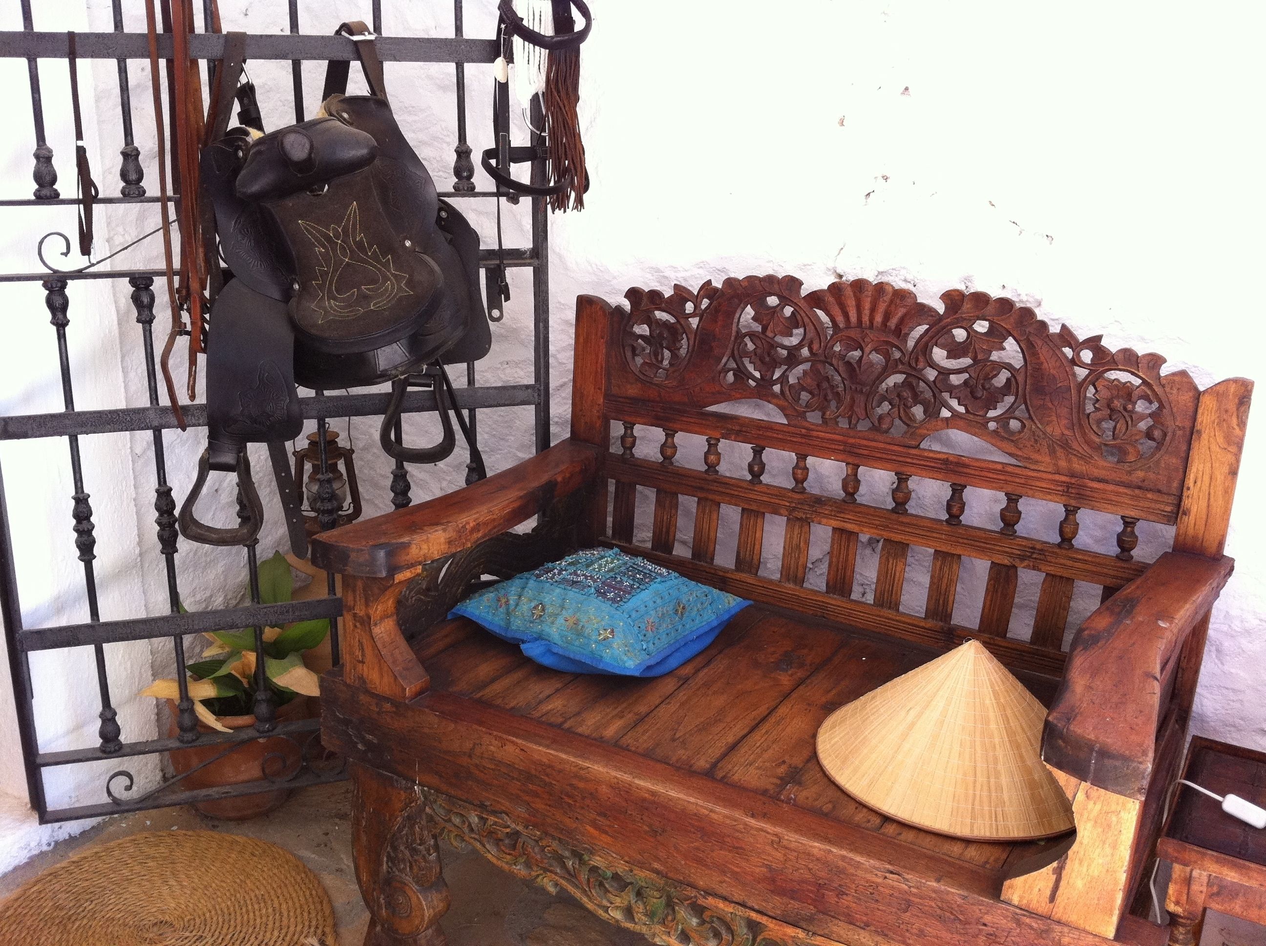 A wooden bench with a decorative backrest, a blue cushion, and a straw hat placed on it.