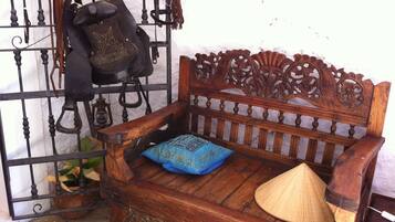 A wooden bench with a decorative backrest, a blue cushion, and a straw hat placed on it.