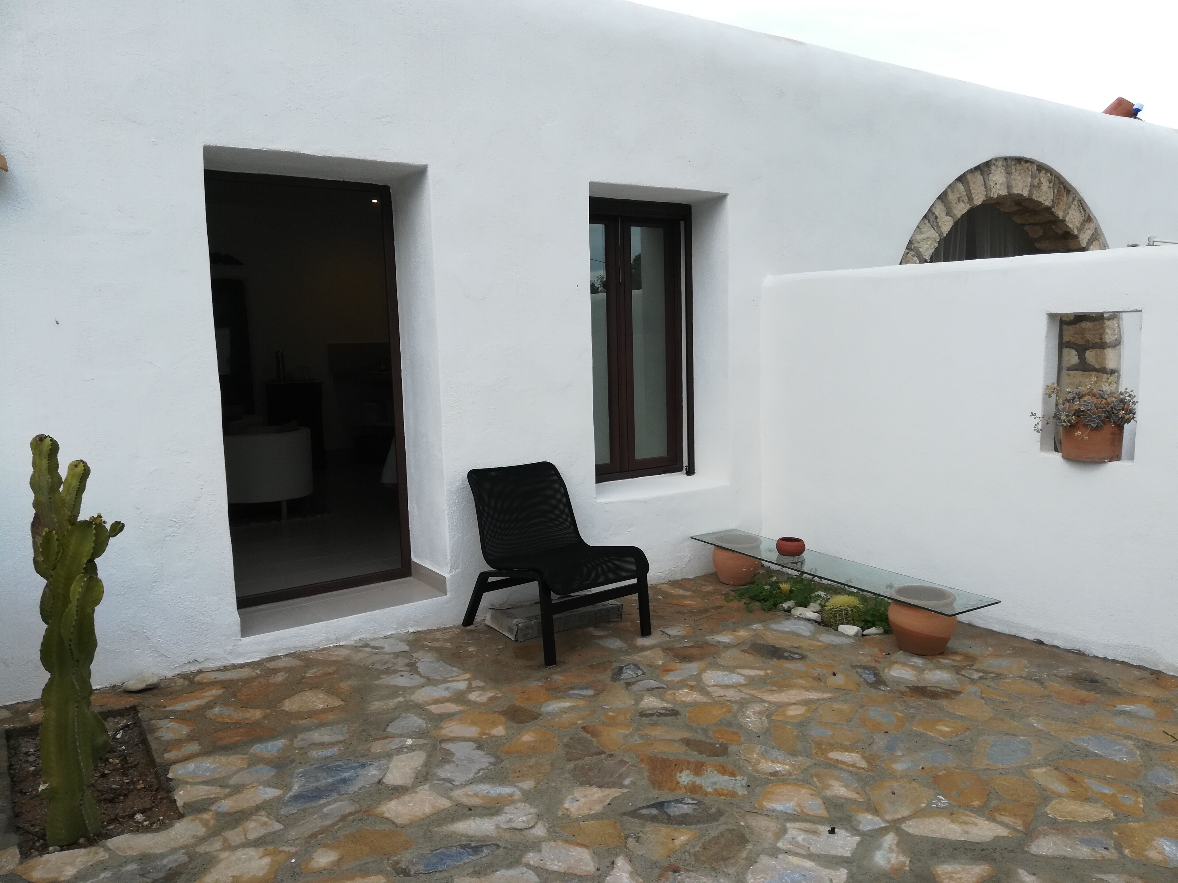 Une terrasse dallée de pierres, avec une chaise noire, un cactus et une petite table sur laquelle est posée une plante en pot.
