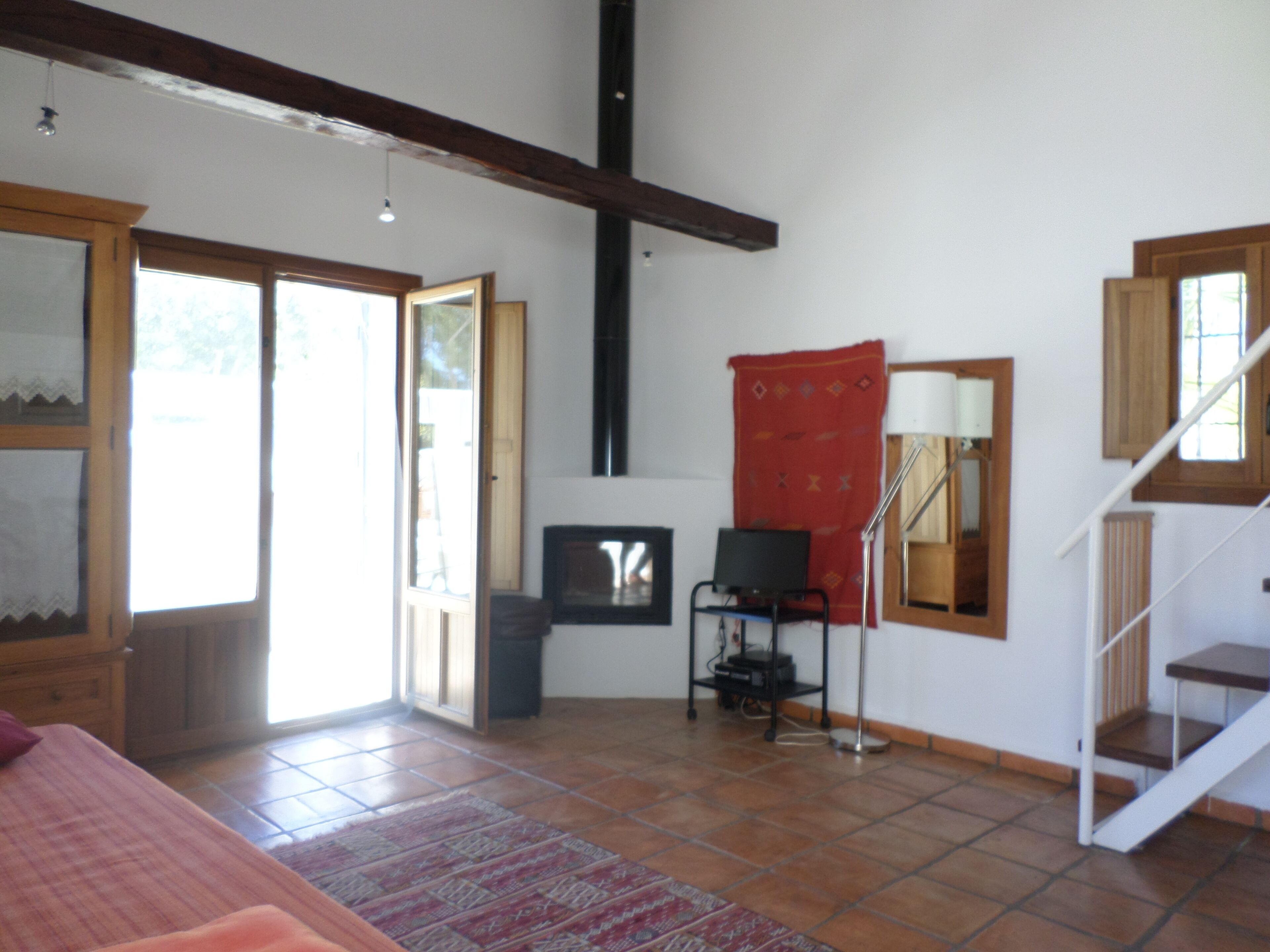 A room with a bed, a desk, a chair, a lamp, a red tapestry, and a staircase.