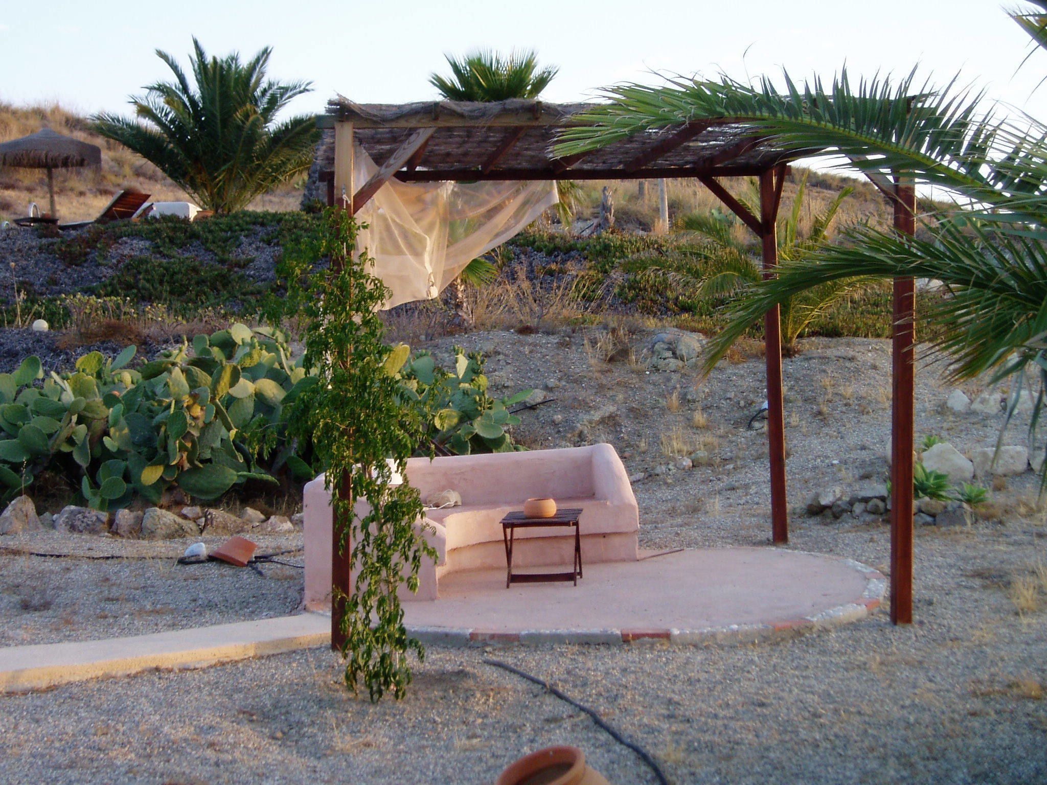 A cozy outdoor seating area with a cushioned bench, a small table, and a pergola structure.