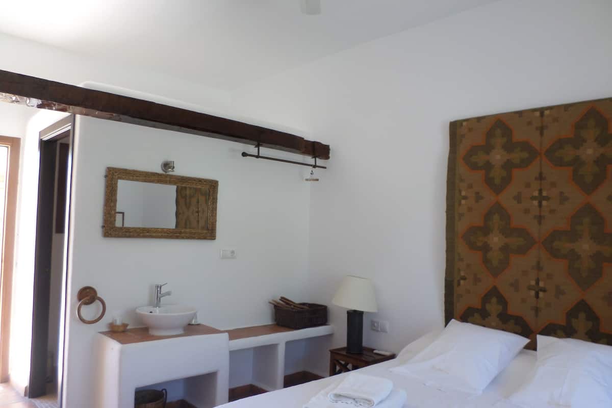 A hotel room with a bed, a sink, a mirror, and a patterned wall.