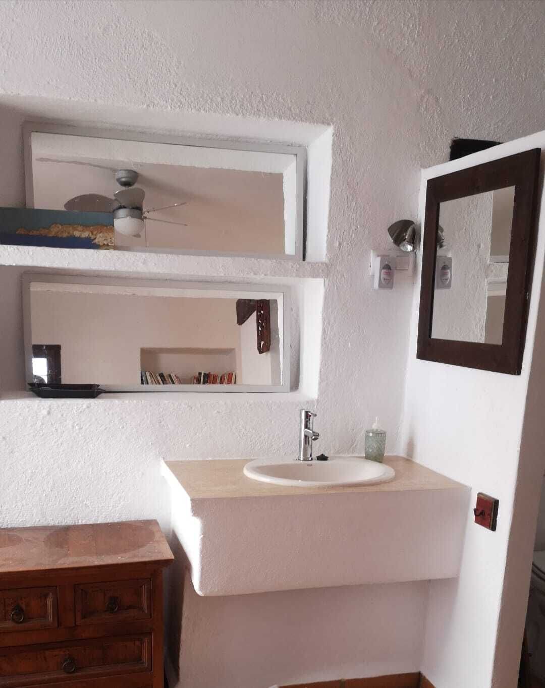 A bathroom with a white sink, two mirrors, a wooden cabinet, and a ceiling fan.