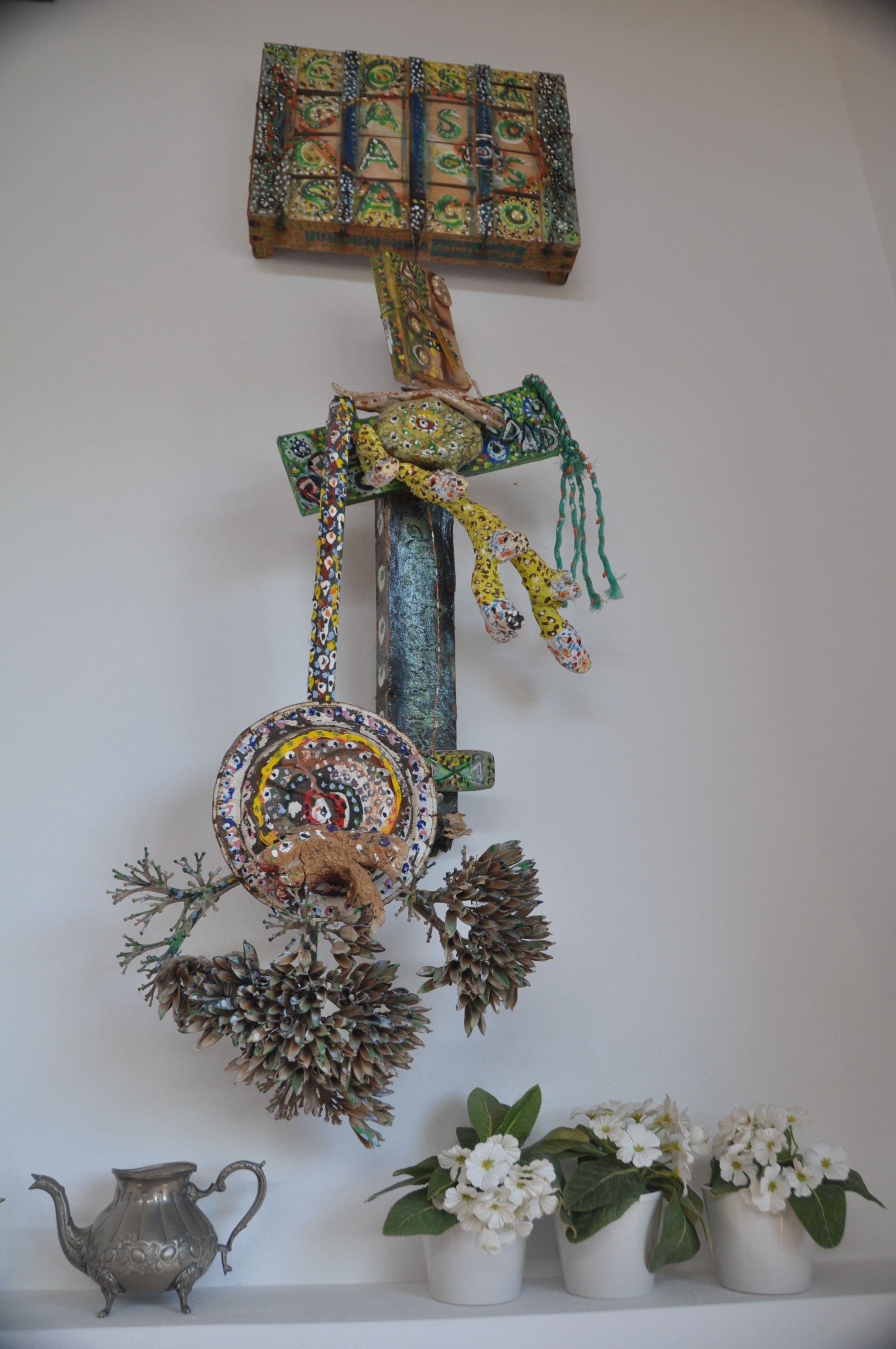 En dekorativ väggdekoration med ett hängande ornament, en liten kruka och en kanna.