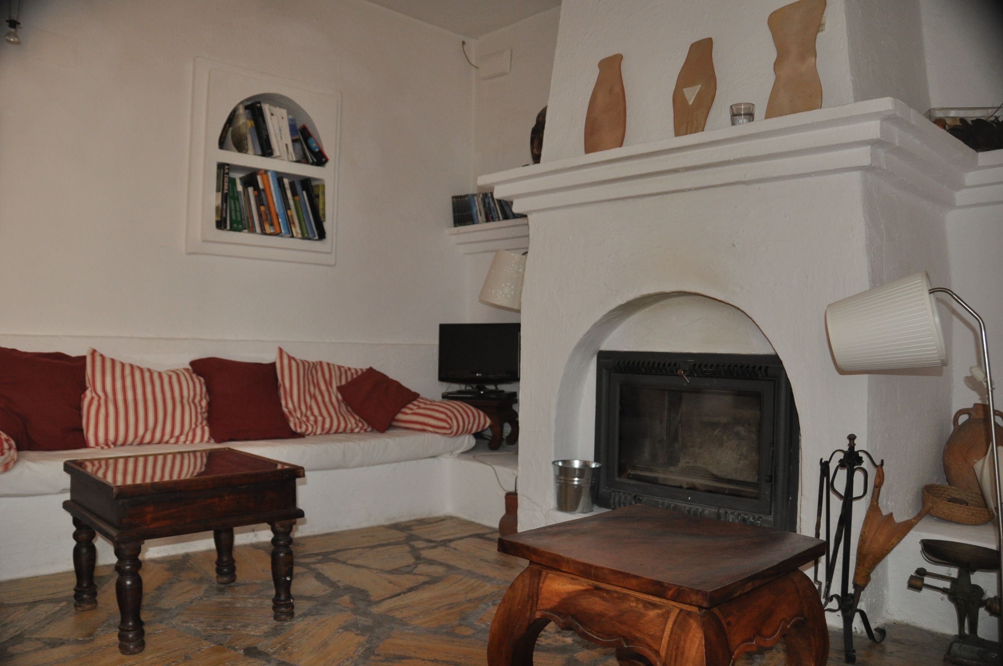 A cozy living room with a fireplace, a sofa with striped pillows, a wooden coffee table, and a bookshelf.