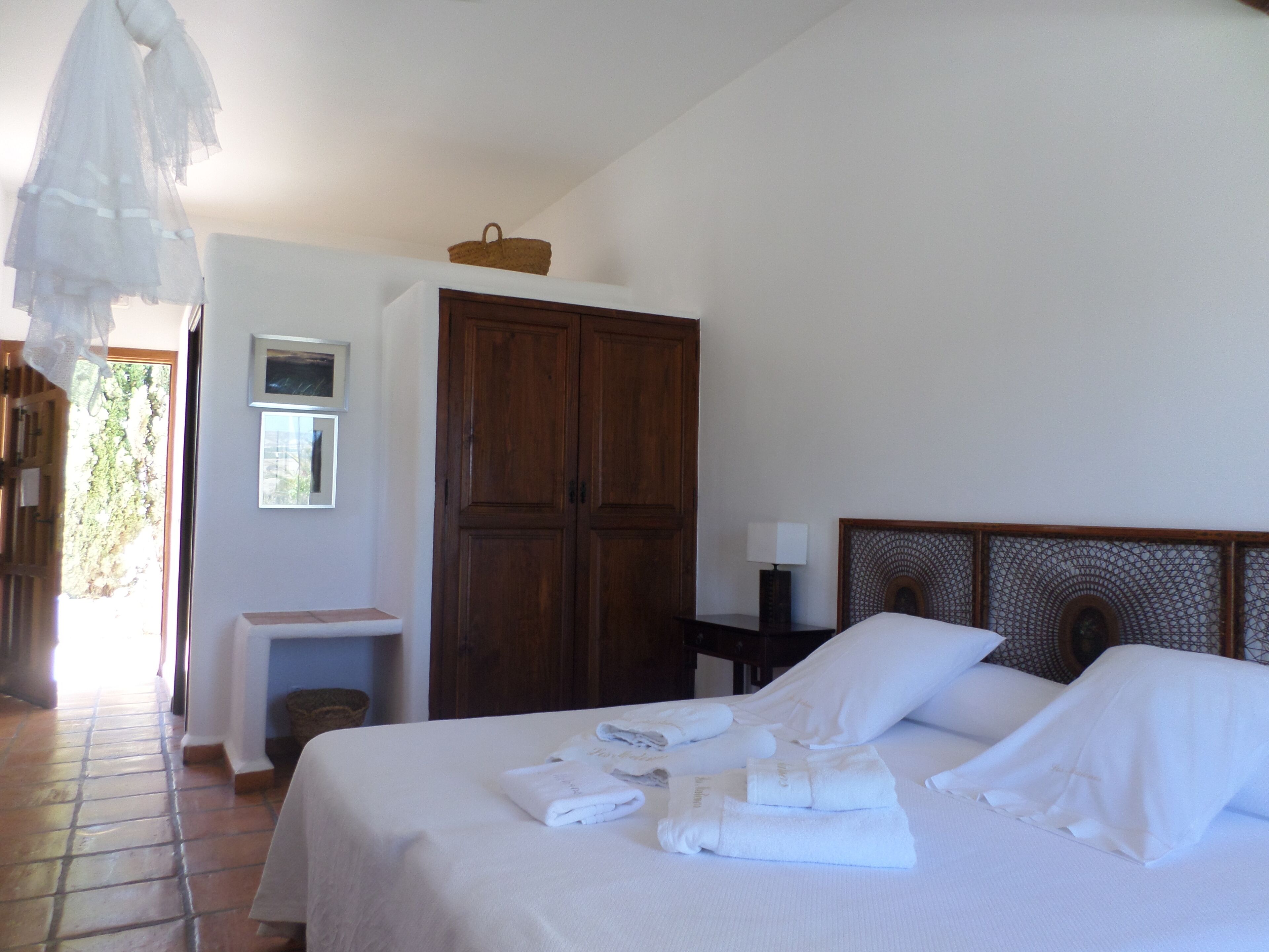 Habitación de hotel con cama, armario, mesita de noche con lámpara y ventana con vista a zonas verdes.