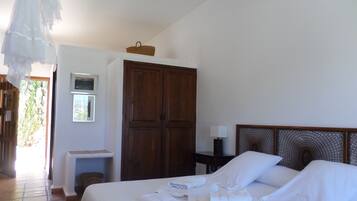 Habitación de hotel con cama, armario, mesita de noche con lámpara y ventana con vista a zonas verdes.